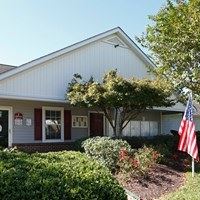 A white house with a red door and a tree in front.